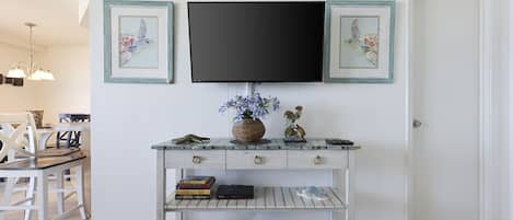 Una consola blanca con un televisor de pantalla plana encima, flanqueada por dos cuadros enmarcados.