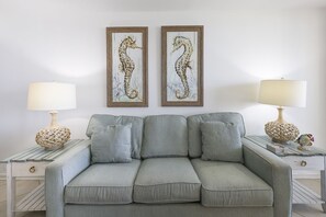 A grey sofa with cushions, two framed seahorse paintings, and two lamps on either side. - Phoenix Iii 3013 1 Bedroom Condo (Orange Beach)