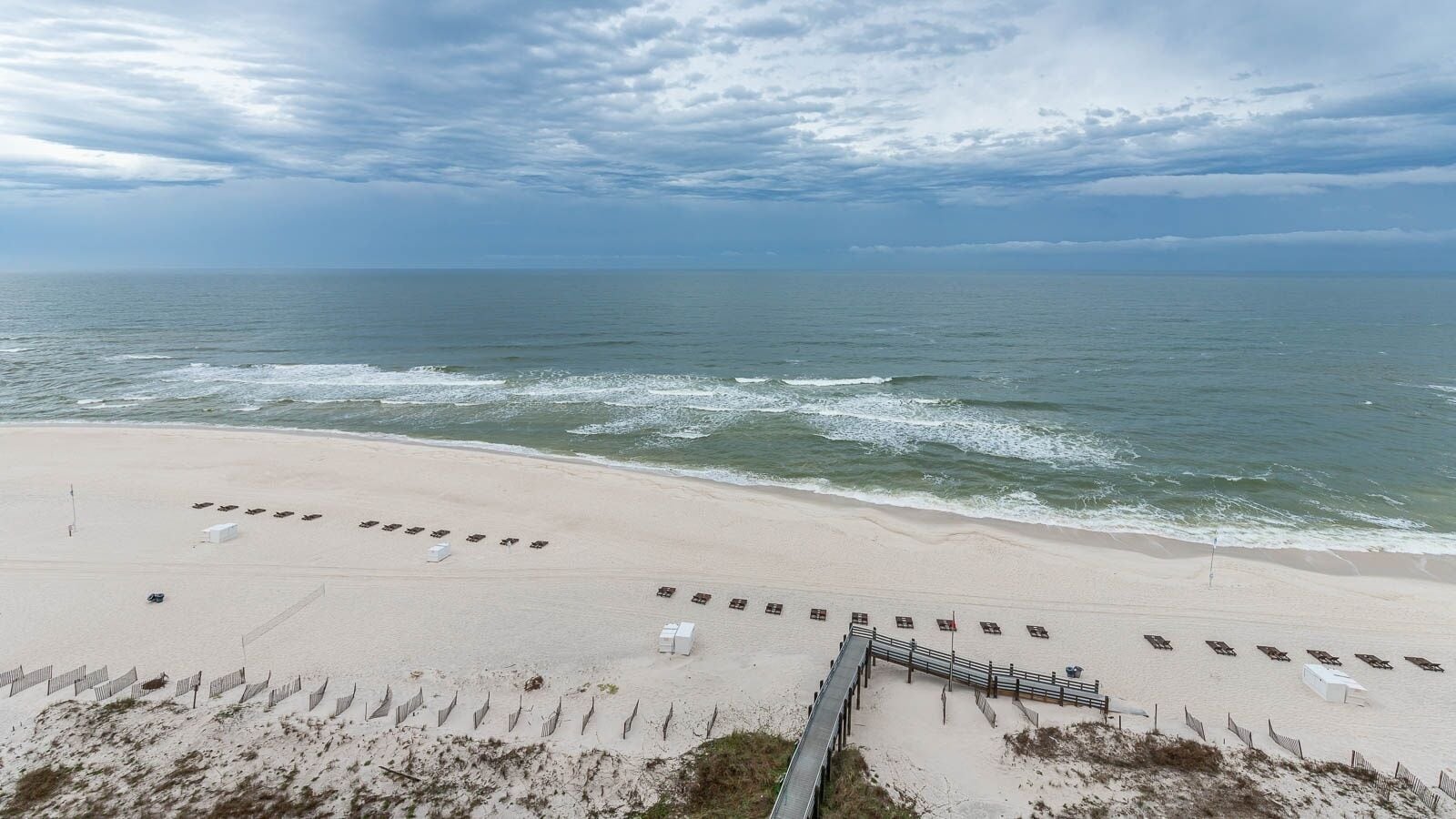 A beach with a wooden walkway leading to a row of beach chairs and umbrellas.