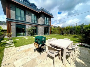 Une maison moderne dotée d’un patio comprenant un barbecue, du mobilier d’extérieur et une pelouse bien entretenue.