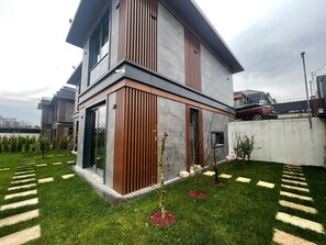 Une maison moderne à deux étages, dotée d’un toit plat, de grandes fenêtres et d’une pelouse bien entretenue agrémentée de pierres plates servant de pas japonais.