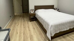 A bedroom with a wooden floor, a bed with a white quilt, a bedside table with a lamp, and a door in the background. - 4-bedroom house in lovely İstanbul with forest view.Nearest Istanbul Airport. (Bolluca)