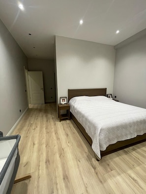 A bedroom with a wooden floor, a bed with a white quilt, a bedside table with a lamp, and a door in the background. - 4-bedroom house in lovely İstanbul with forest view.Nearest Istanbul Airport. (Bolluca)