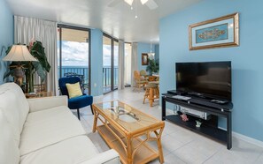 Ein Wohnzimmer mit einer Couch, Sesseln, einem Fernseher und einem Balkon mit Blick.