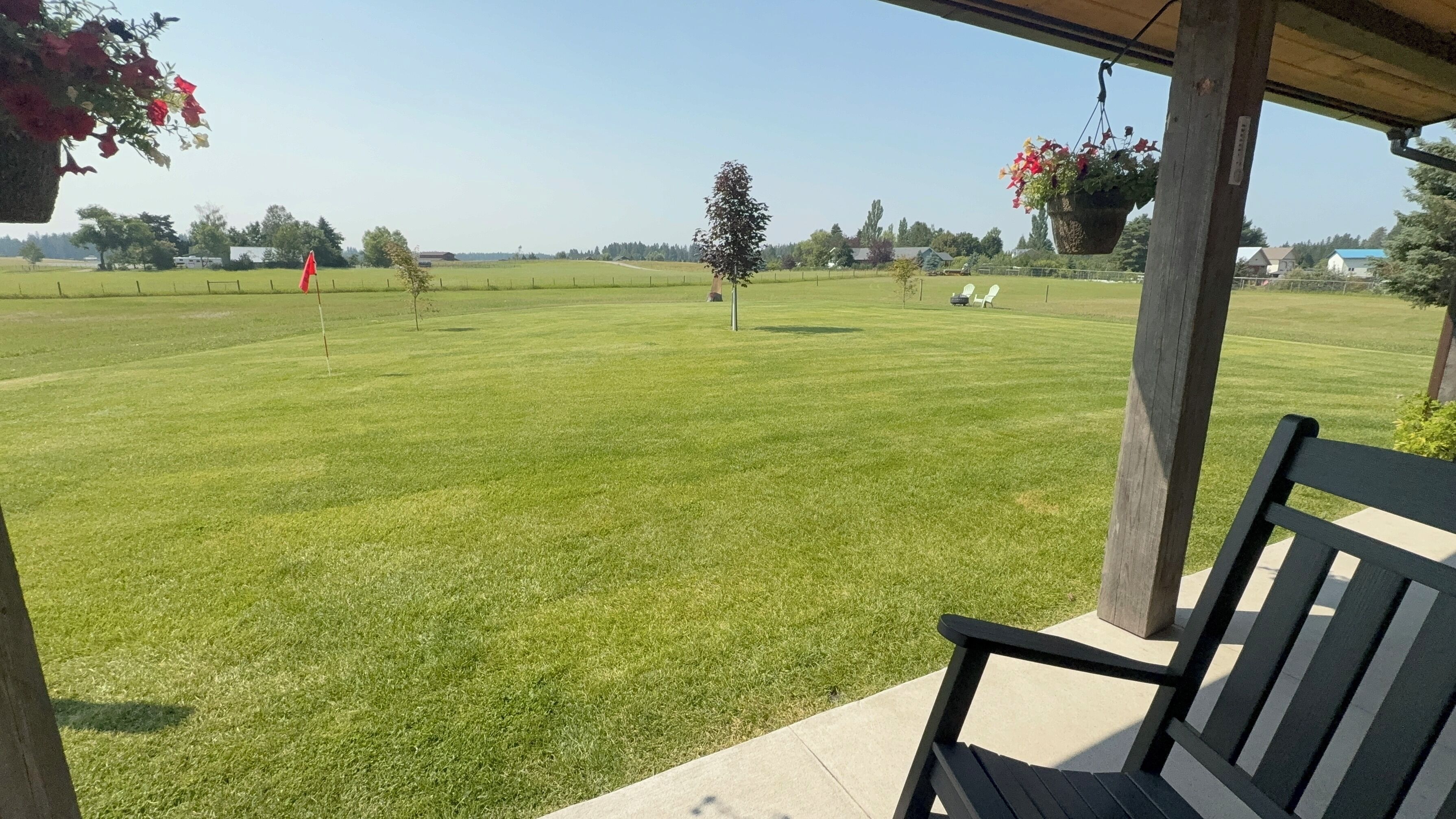 A grassy outdoor area with a wooden bench and hanging flower baskets.