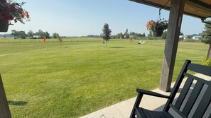 A grassy outdoor area with a wooden bench and hanging flower baskets.