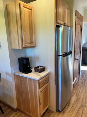 A kitchen with wooden cabinets, a stainless steel refrigerator, a coffee maker, and a basket on the countertop. - The Outback Cabin. With jaw dropping mountain views and Private space (Columbia Falls)