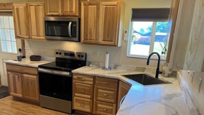 A kitchen with wooden cabinets, a stainless steel microwave, a stove, and a sink.