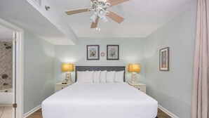 Ein Schlafzimmer mit einem Bett, Nachttischen, Lampen, einem Deckenventilator und gerahmten Bildern an der Wand.
