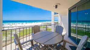 Ein Balkon mit Tisch und Stühlen, der Blick auf einen Strand mit Sonnenschirmen und einem Steg freigibt.