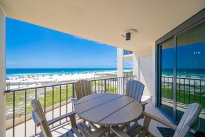 A balcony with a table and chairs, overlooking a beach with umbrellas and a pier. - Phoenix Iii 3023 1 Bedroom Condo (Orange Beach)