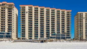 Ein Hochhaus-Hotel mit mehreren Balkonen, ein Sandstrand im Vordergrund und ein klarer, blauer Himmel.