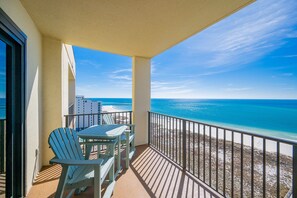 A balcony with a table and chairs, overlooking a beach and ocean. - Phoenix Vii 71506 2 Bedroom Condo (Orange Beach)