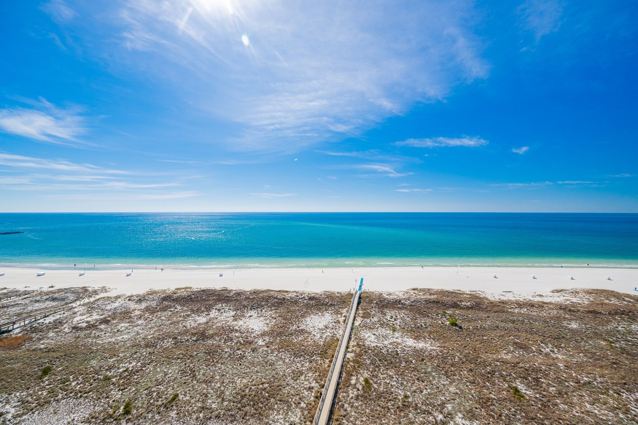 A beach with a clear sky, a sandy shore, and a wooden boardwalk leading to the water.