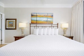 A hotel room with a large bed, two bedside tables with lamps, a framed picture on the left wall, and a painting above the bed. - Phoenix Vii 71506 2 Bedroom Condo (Orange Beach)