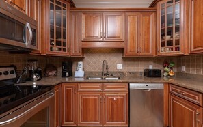 A kitchen with wooden cabinets, a microwave, a coffee maker, a toaster, and a dishwasher. - Phoenix Vii 7012 3 Bedroom Condo (Orange Beach)