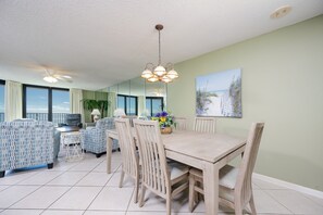 A dining area with a wooden table and chairs, a ceiling fan, and a view of the ocean through large windows. - Phoenix Vii 7608 3 Bedroom Condo (Orange Beach)