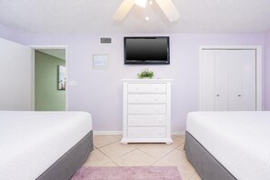 A bedroom with two beds, a white dresser, a flat-screen TV, and a door. - Phoenix Vii 7608 3 Bedroom Condo (Orange Beach)