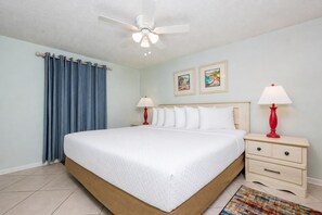 Ein Hotelzimmer mit einem Bett, zwei Nachttischen mit Lampen, einem Deckenventilator und zwei gerahmten Bildern an der Wand.