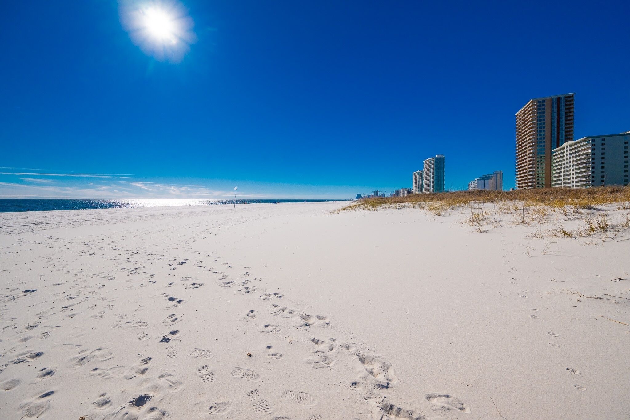 A sandy beach with footprints leading towards the ocean and buildings in the background.