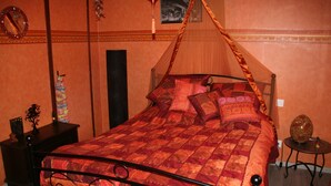 A bedroom with a four-poster bed, a nightstand, a small table, and a decorative item on the nightstand.
