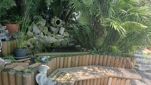 A wooden bench with a stone sculpture, surrounded by a wooden fence and various plants.
