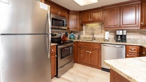 A kitchen with wooden cabinets, stainless steel appliances, a microwave, stove, oven, and a coffee maker. - Phoenix Vii 7813 2 Bedroom Condo (Orange Beach)