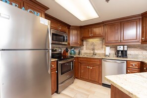 A kitchen with wooden cabinets, stainless steel appliances, a microwave, stove, oven, and a coffee maker. - Phoenix Vii 7813 2 Bedroom Condo (Orange Beach)
