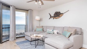 A modern living room with a grey sectional sofa, a small round coffee table, and a view of the ocean through large sliding glass doors. - Phoenix Vii 7813 2 Bedroom Condo (Orange Beach)