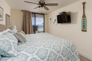 Une chambre avec un lit, un ventilateur de plafond, une télévision et une vue sur la plage, accessible par une porte coulissante.