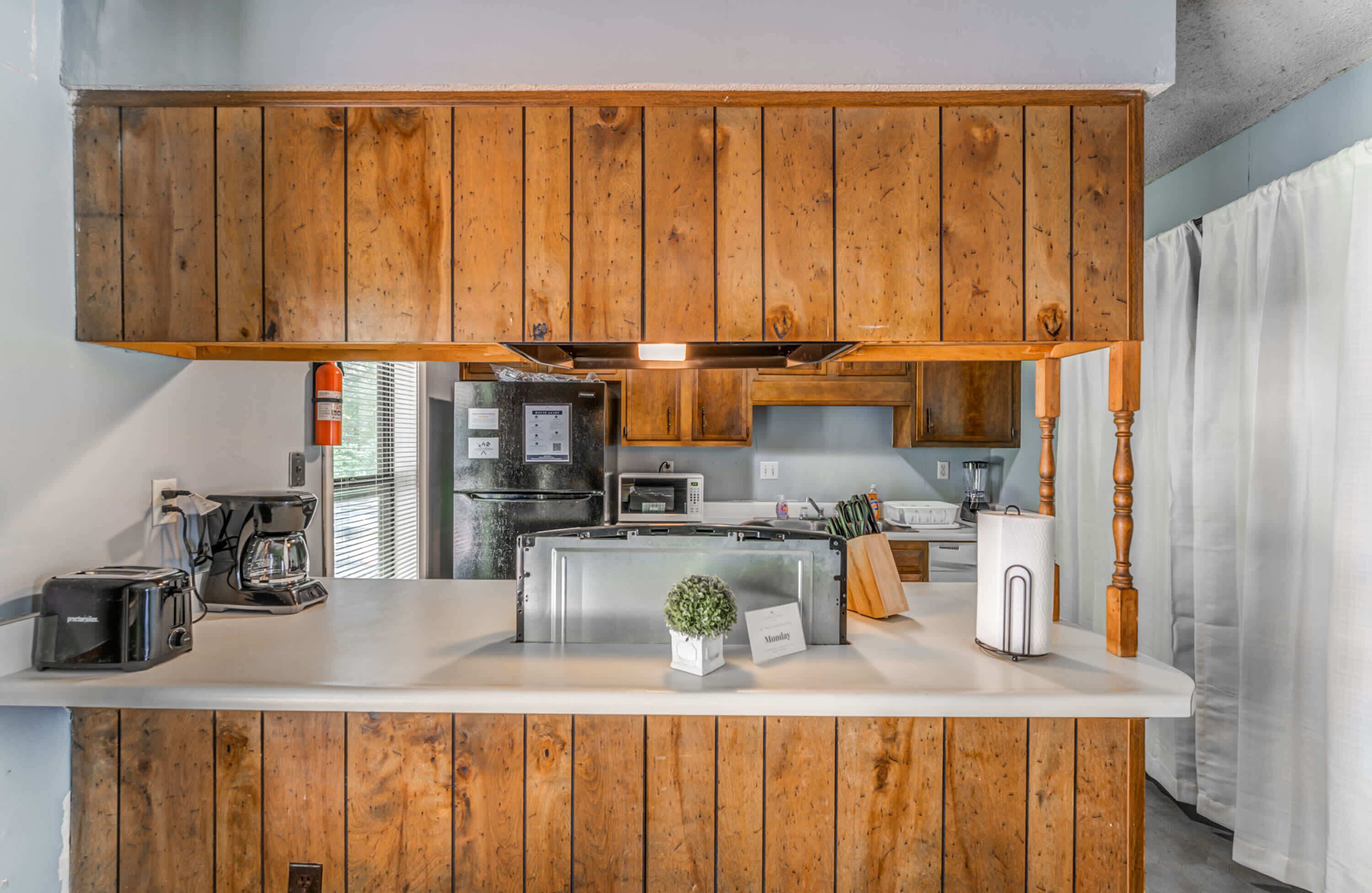 A kitchen with wooden cabinets, a stainless steel refrigerator, a coffee maker, and a small potted plant on the counter.