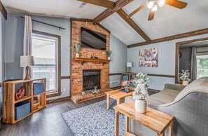 A living room with a brick fireplace, wooden beams, a sofa, a coffee table, and a rug. - Near Dining & MEM - Hickory Hill Home (Memphis)