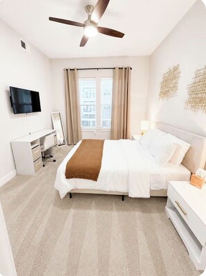 A bedroom with a bed, a desk, a TV, a ceiling fan, and a window with curtains. - Luxury 2BR • King Suite • Minutes to PGA, Universal & The Star (Frisco)