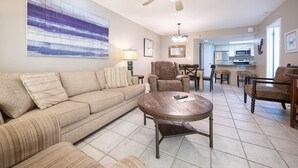A living room with a sofa, armchairs, a coffee table, a ceiling fan, and a kitchen in the background. - Phoenix Vii 7306 2 Bedroom Condo (Orange Beach)