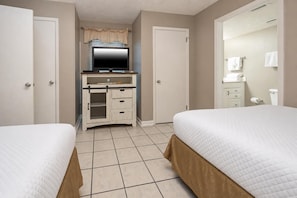 Ein Hotelzimmer mit zwei Betten, einem Fernseher, einem Schreibtisch und einem Badezimmer.