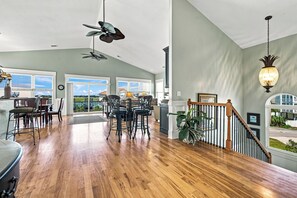 Ein geräumiger Wohnbereich mit Holzboden, einem Esstisch mit Stühlen, einem Deckenventilator und einer Treppe mit Geländer.