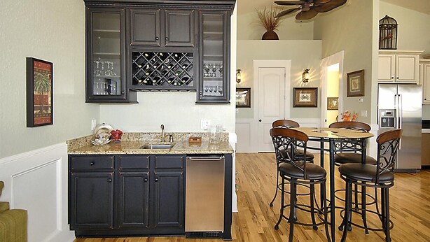 A kitchen with dark cabinetry, a wine rack, and a dining area with chairs and a table. - High Cotton: Inlet Views, Private Dock, Pool & Easy Beach Access (Murrells Inlet)