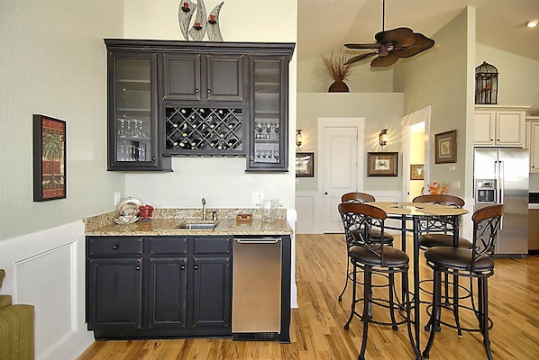A kitchen with dark cabinetry, a wine rack, and a dining area with chairs and a table. - High Cotton: Inlet Views, Private Dock, Pool & Easy Beach Access (Murrells Inlet)