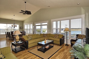 A spacious living room with a high ceiling, a sectional sofa, a dining table with chairs, and large windows with blinds. - High Cotton: Inlet Views, Private Dock, Pool & Easy Beach Access (Murrells Inlet)
