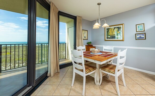 A dining area with a view of the ocean, white chairs, a wooden table, and a chandelier. - Phoenix Vii 7202 1 Bedroom Condo (Orange Beach)