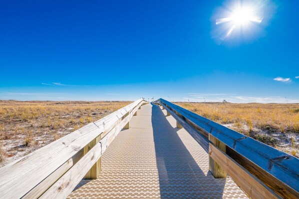 A wooden boardwalk extending into a flat landscape with a clear blue sky. - Phoenix Vii 7202 1 Bedroom Condo (Orange Beach)