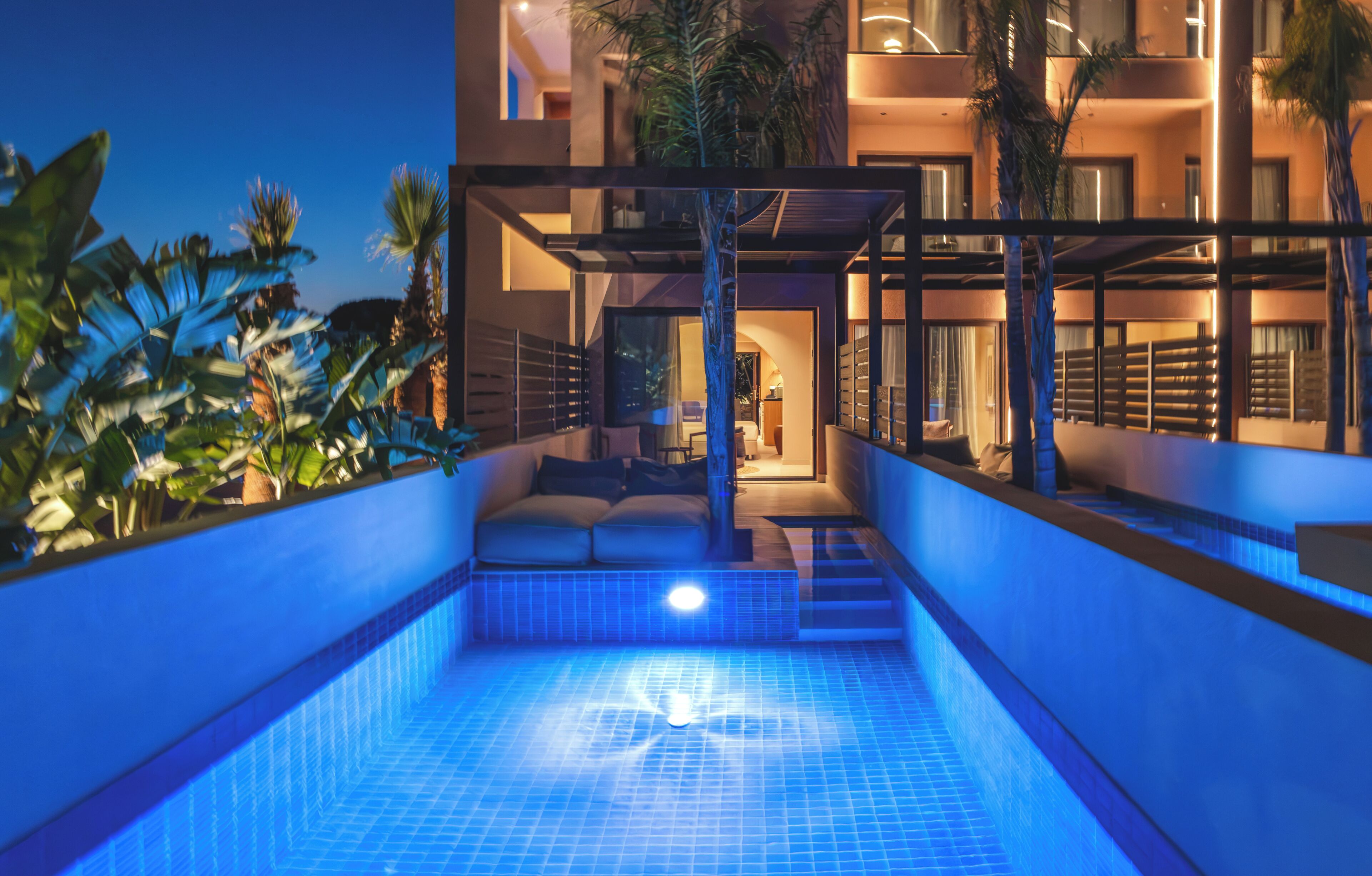 Een modern hotel met een zwembad, terras en een goed verlichte entree.