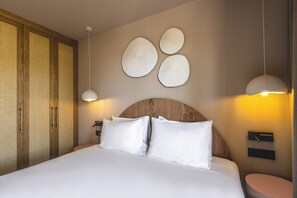 A neatly made bed with white linens, a wooden headboard, and a wall-mounted light fixture.