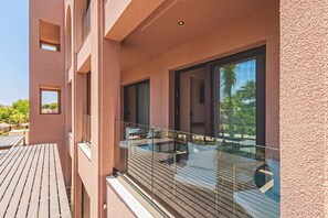 A balcony with a glass railing, wooden flooring, and outdoor furniture.