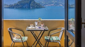 Ein Balkon mit zwei Stühlen, einem Tisch und Blick auf einen See mit Booten und einer entfernten Insel.