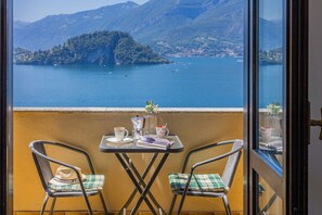 Ein Balkon mit zwei Stühlen, einem Tisch und Blick auf einen See mit Booten und einer entfernten Insel.
