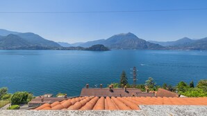 Blick auf einen See mit Bergen im Hintergrund, ein Ziegeldach und ein klarer Himmel.