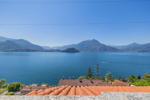Blick auf einen See mit Bergen im Hintergrund, ein Ziegeldach und ein klarer Himmel.