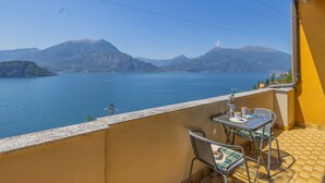Ein Balkon mit Tisch und Stühlen mit Blick auf einen See, in der Ferne Berge.