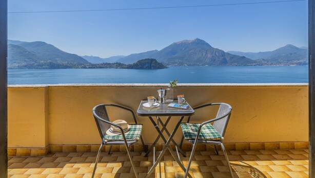 Ein Balkon mit zwei Stühlen und einem Tisch, mit Blick auf ein Gewässer und entfernte Berge.